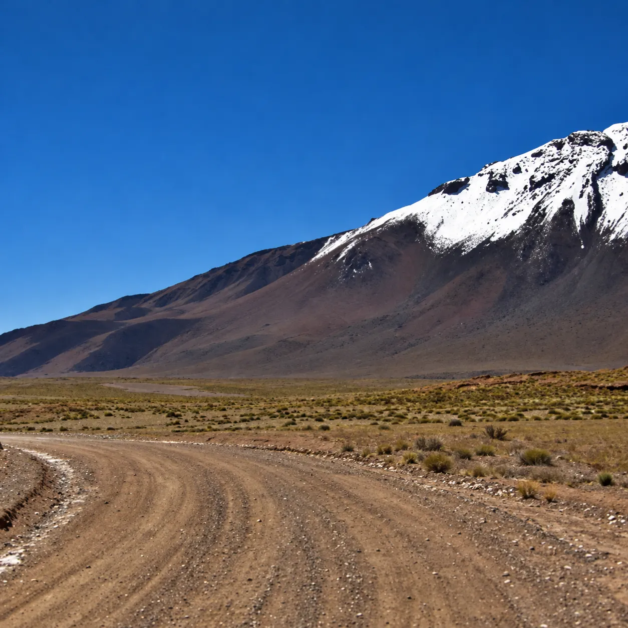 Camino de ripio hacia el volcán Tuzgle con la cumbre nevada, Puna de Jujuy a 4.000 msnm